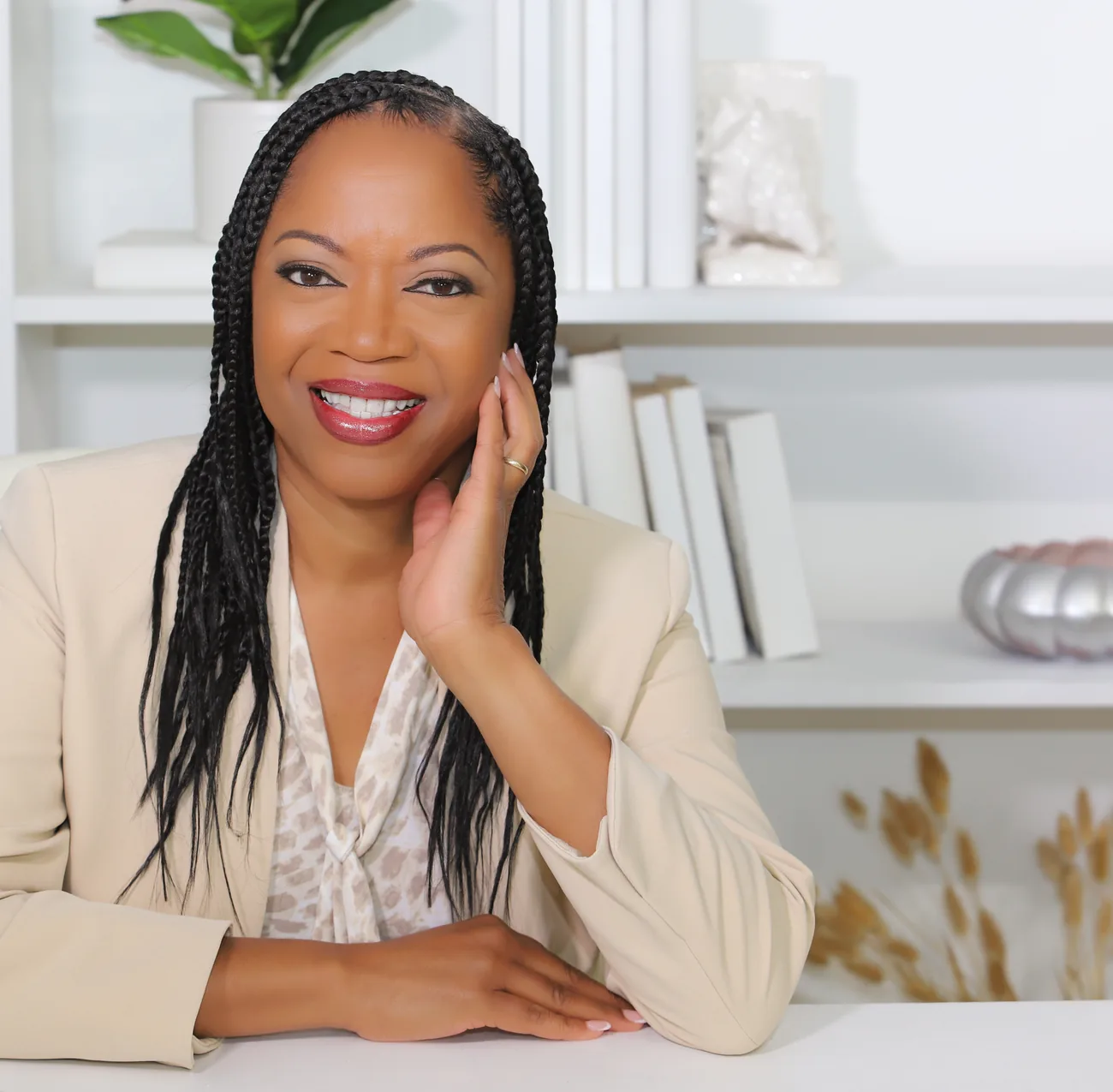 Dinah Rainey in a beige blazer, listening, hand resting on her cheek.